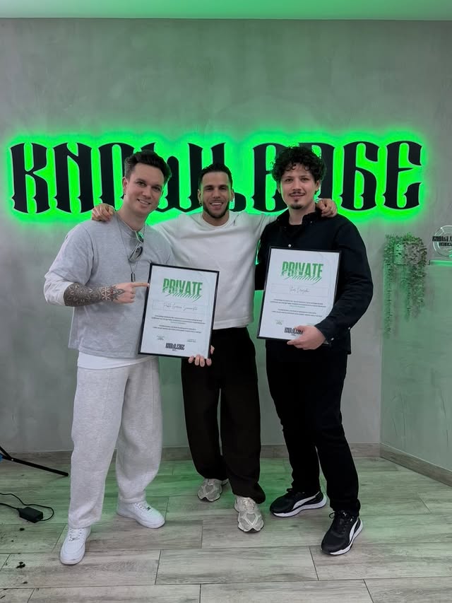 Alumnos de Knowledge Academy BCN con sus certificados frente al logo iluminado de la academia